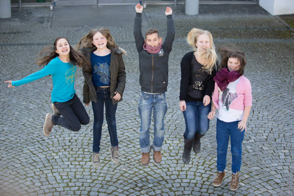 Fünf Schüler stehen auf einem gepflasterten Platz und springen in die Luft.