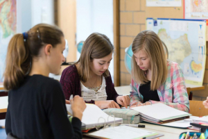 Drei Schülerinnen sitzen an einem Gruppentisch. Auf dem Tisch befinden sich Ordner und Mäppchen.