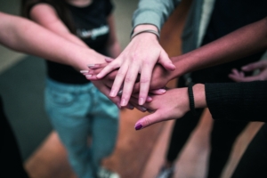 Foto von fünf Händen, die von fünf Personen übereinander gehalten werden.