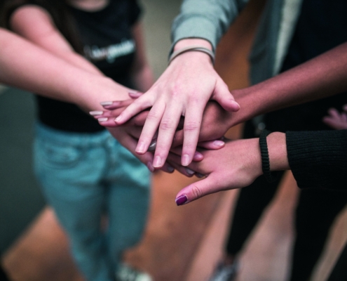 Foto von fünf Händen, die von fünf Personen übereinander gehalten werden.