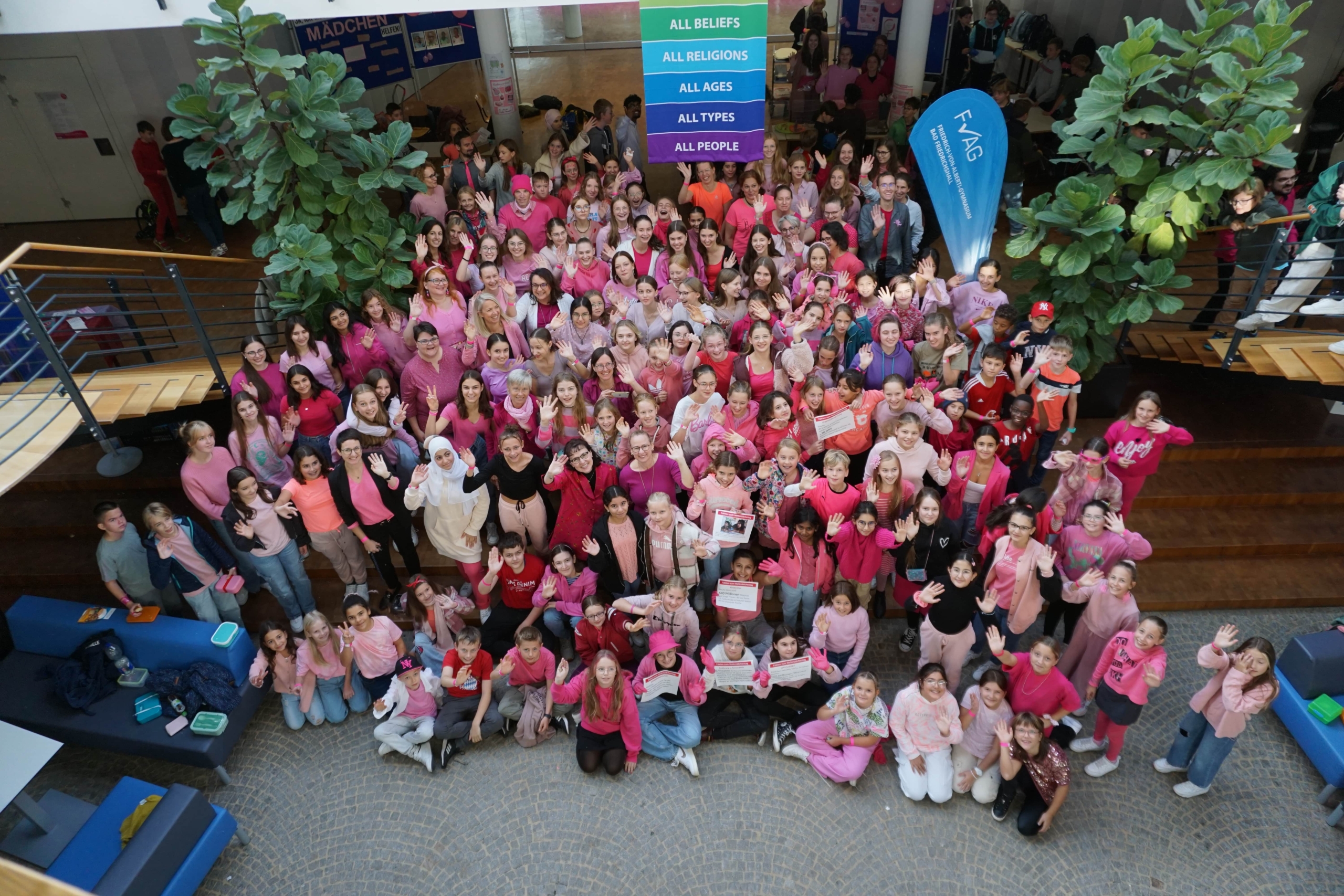 Foto von der Empore hinunter in das Foyer das Schule. Zu sehen sind unzählige Schülerinnen und Schüler mit pinker und rosafarbener Bekleidung.