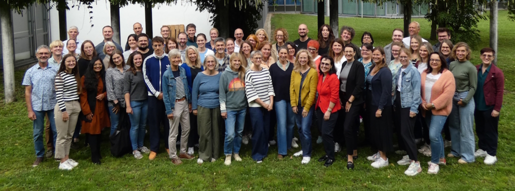 Abgebildet ist das Kollegium des FvAGs. Im Hintergrund sind Bäume und das Schulgebäude erkennbar.