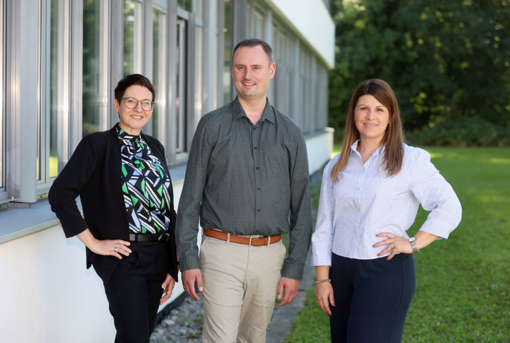 Foto von Fr. Stephan, Hr. Krämer und Fr. Felsinger. Im Hintergrund ein Teil des Schulgebäudes und grüne Wiese/Wald