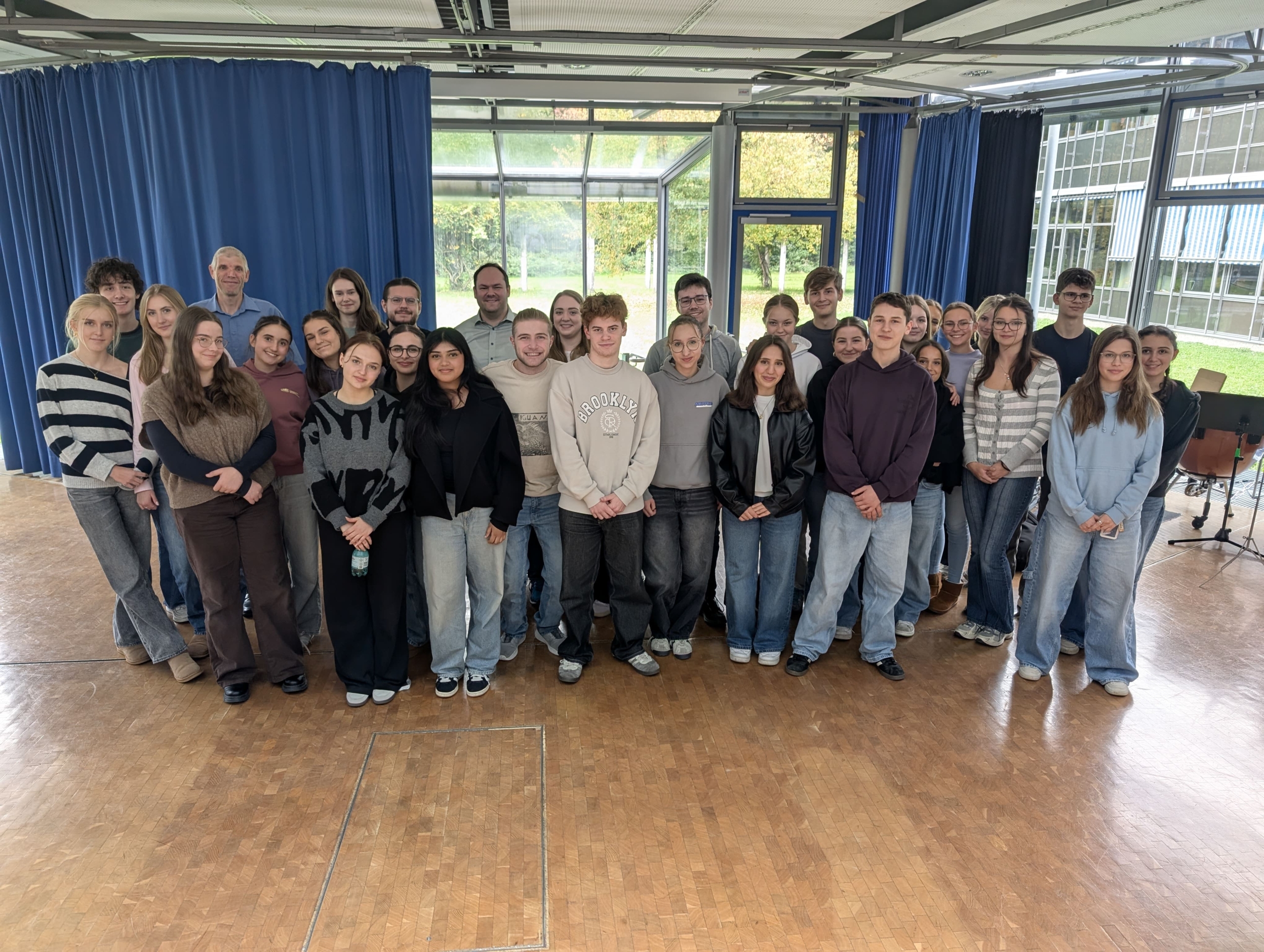 Schülerinnen und Schüler der Kursstufe, Lehrer und Ehemalige stehen als Gruppe in der Aula.