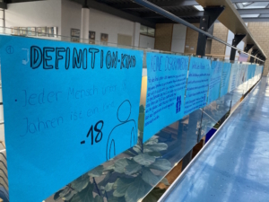 Blaue Plakate zu Kinderrechten an einem Geländer im Schulgebäude.