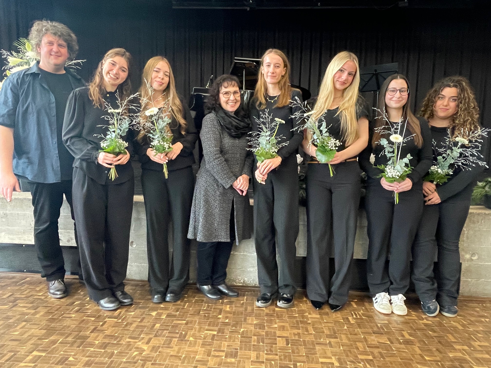 Gruppenfoto von schwarz gekleideten Schülerinnen und Lehrkräften. Die Schülerinnen haben einen kleinen Blumenstrauß in der Hand.