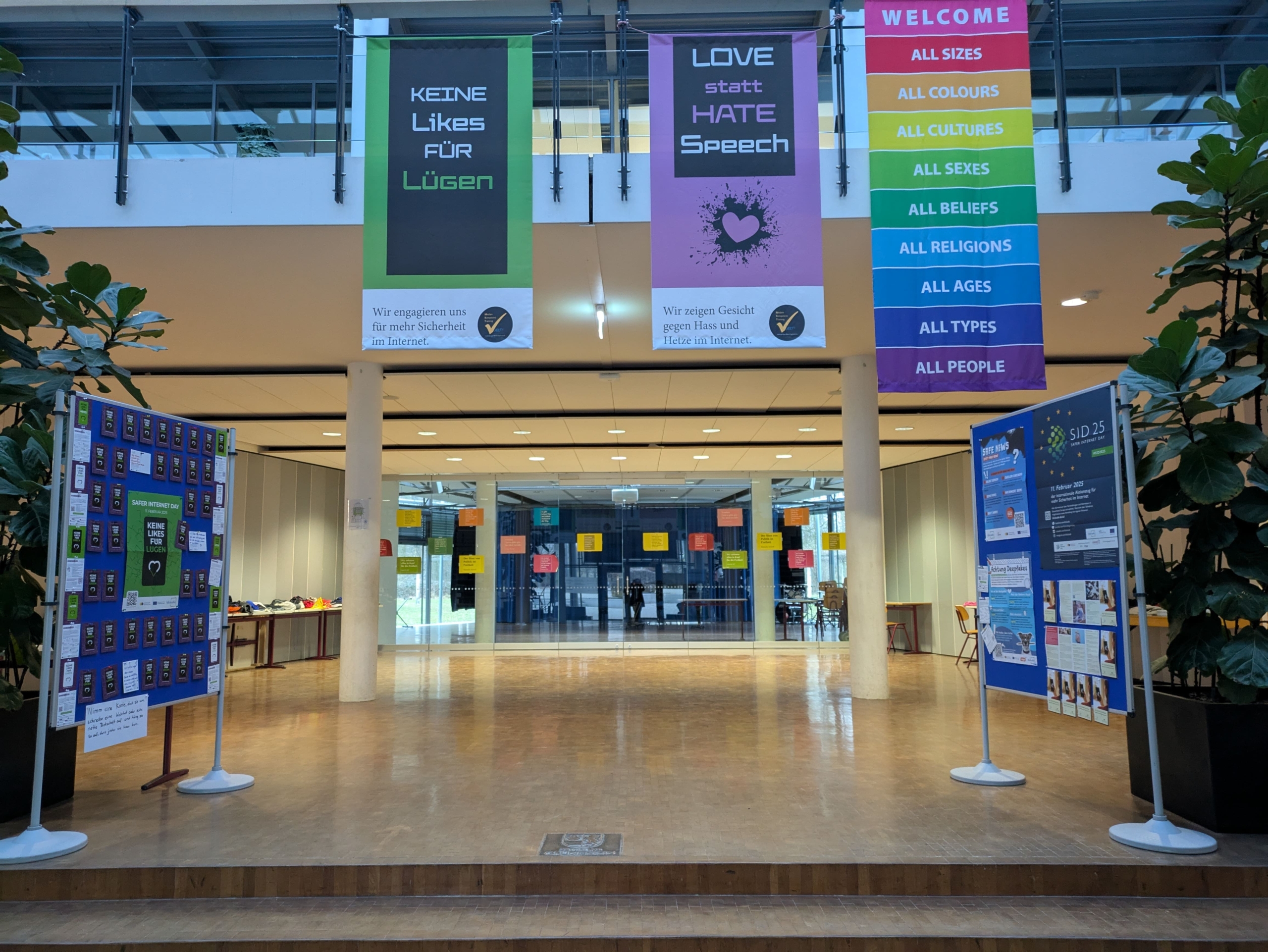 Foto des Foyers. Links und rechts stehen Stellwände mit Plakaten zum Safer Internet Day. Von der Empore hängen drei Banner hinab ins Foyer.