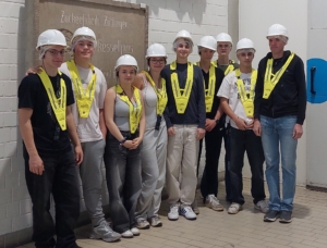 Eine Gruppe Schüler steht zusammen mit einer Lehrkraft vor einer Steintafel mit der Aufschrift Zuckerrübenfabrik Züttlingen.