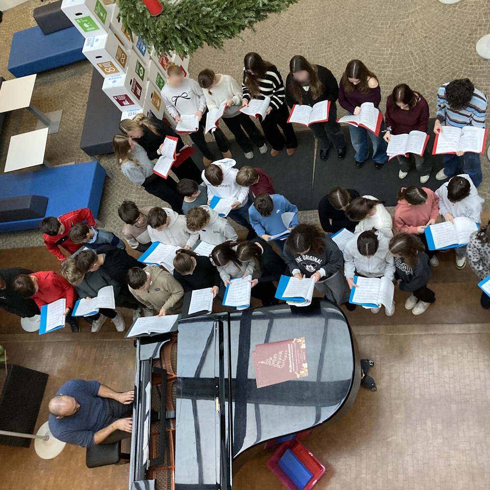 Schüler singen im Foyer, jemand spielt auf dem Flügel.