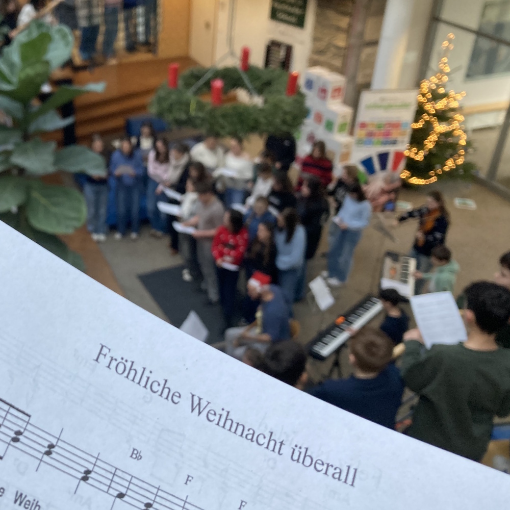 Schüler musizieren im Foyer. Im Vordergrund ist das Liedblatt zu Fröhliche Weihnacht überall.