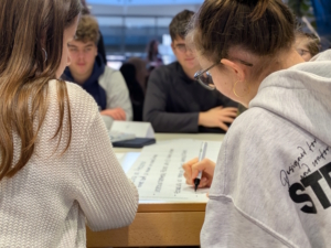 Schüler sitzen um einen Tisch und schreiben etwas.