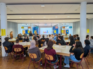 Schüler sitzen um Tische in der Aula.